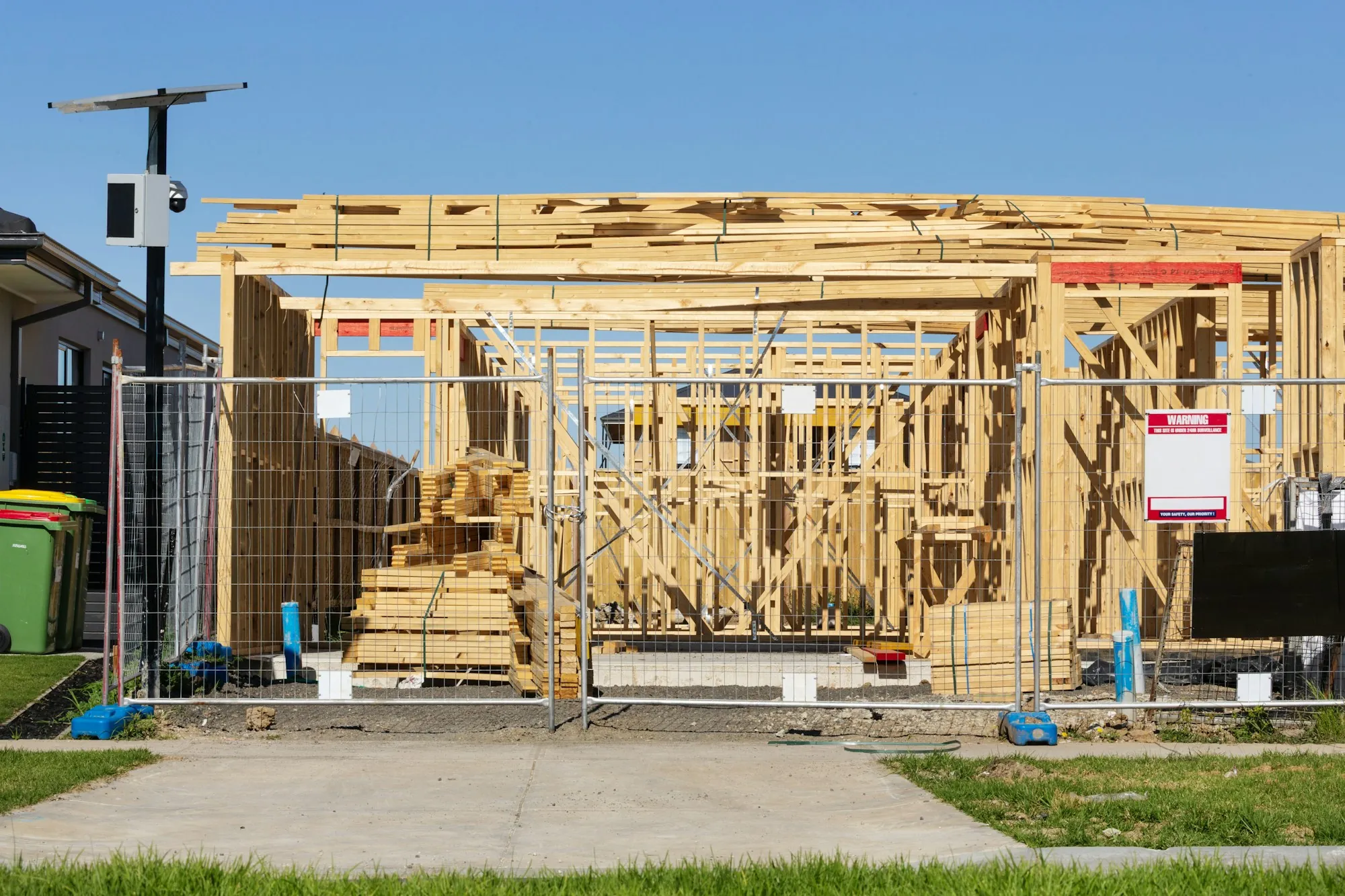 Wooden frame of a new home rising behind site fencing